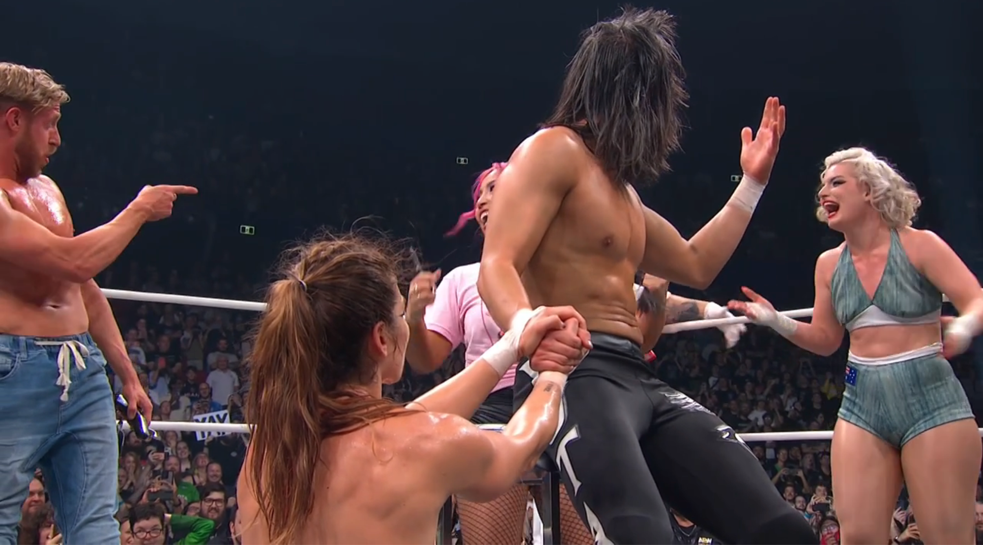 Marina Shafir holds Yuta's hand as he is about to be shaved in the ring, as his opponents laugh it up